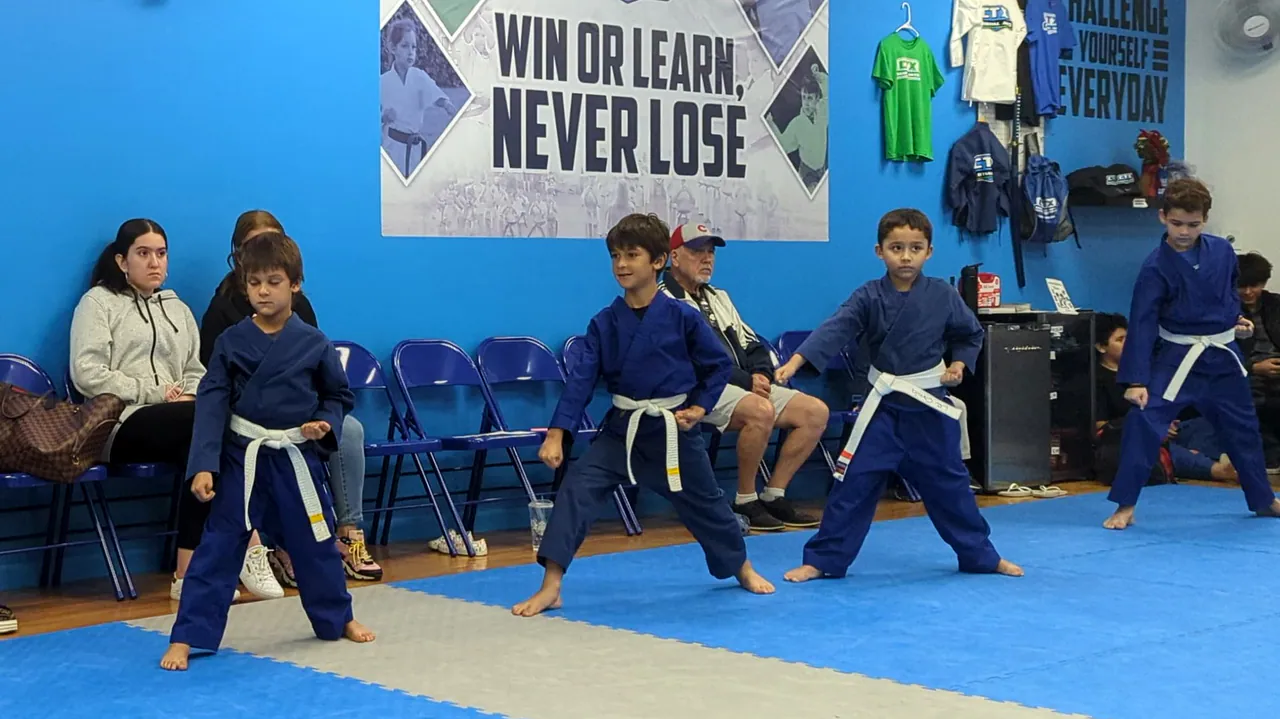 Beginner kids in blue uniforms holding a karate stance in front of the Win or Learn, Never Lose banner