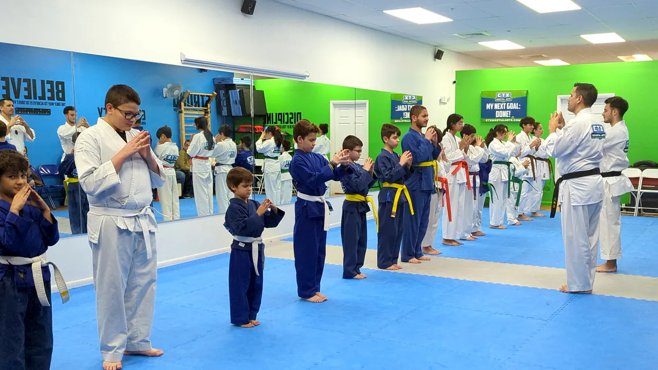 Instructor demonstrating a karate sequence to kids standing in rows by belt color