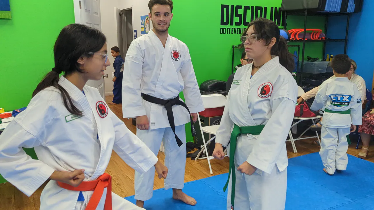 Instructor giving feedback to youth karate students with orange and green belts
