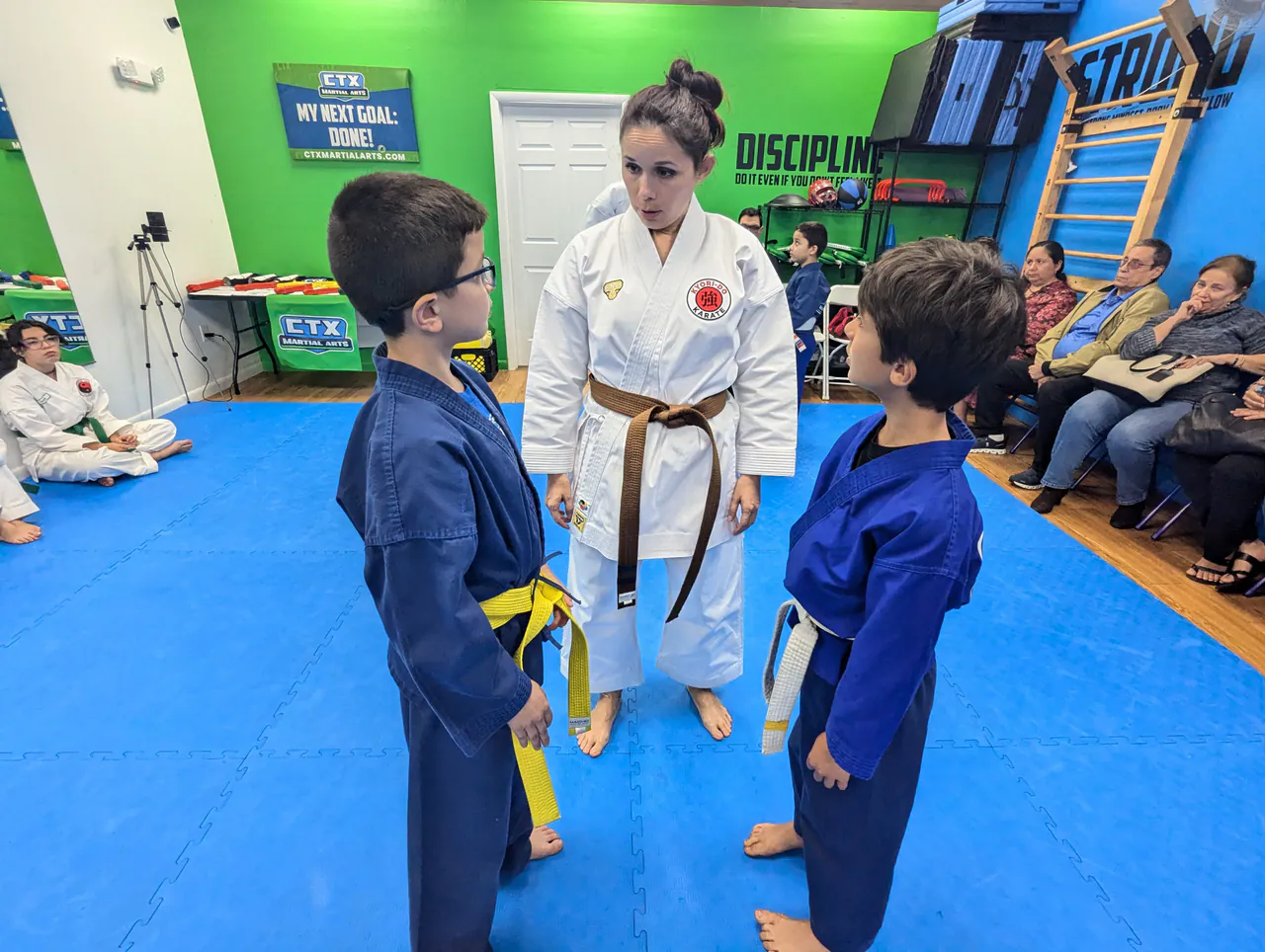 Instructor standing between two kids in blue uniforms during a posture and boundaries exercise