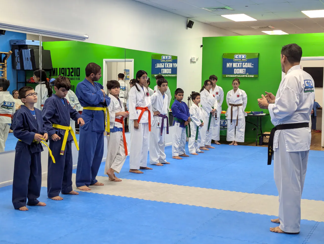 Kids karate class lined up by belt color in the CTX teaching space