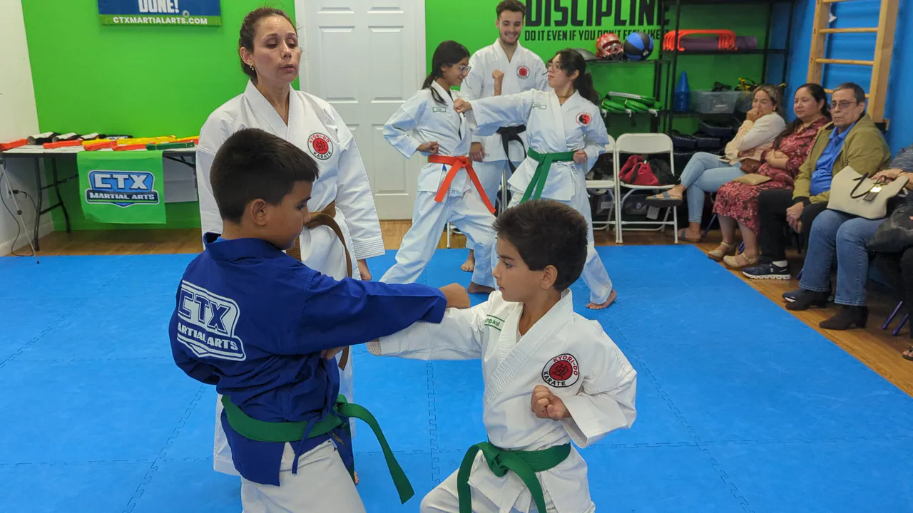 Instructor watching two kids with green belts practice a karate partner drill