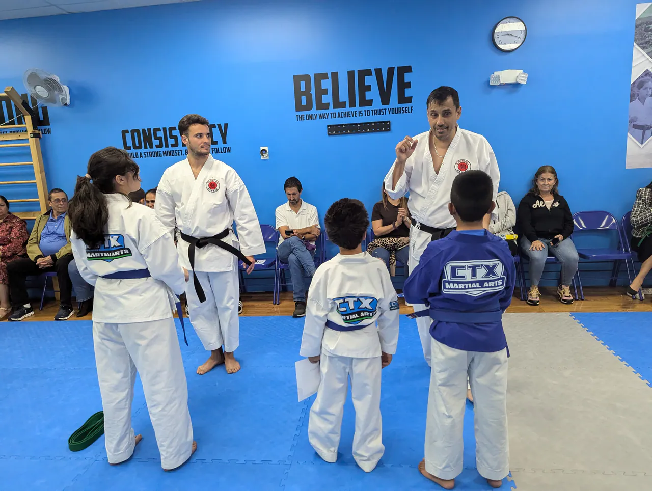 Karate instructors coaching young students in front of the Believe wall at CTX