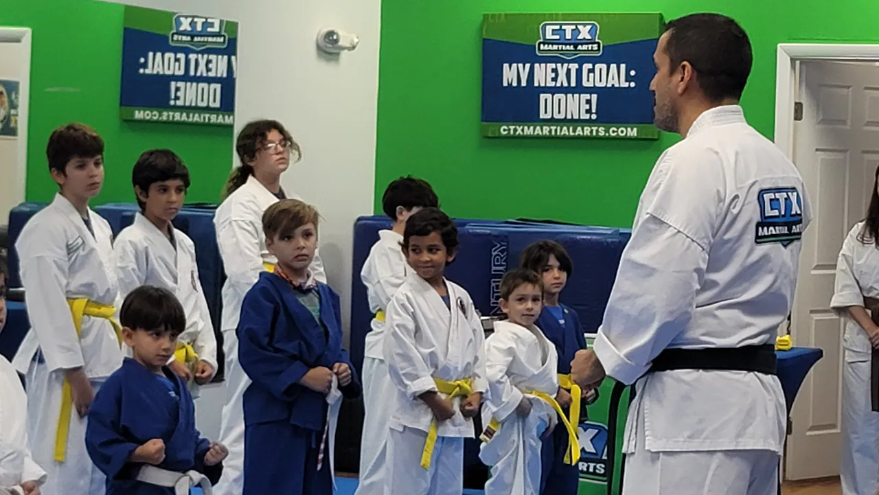 Karate instructor talking with a small group of kids in white and blue uniforms at CTX Martial Arts