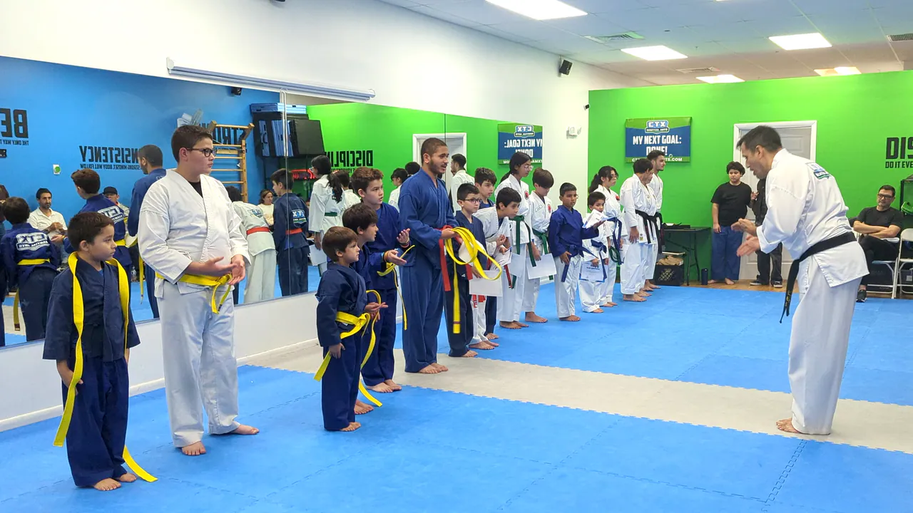 Kids in blue uniforms standing in line and listening to a black belt karate instructor