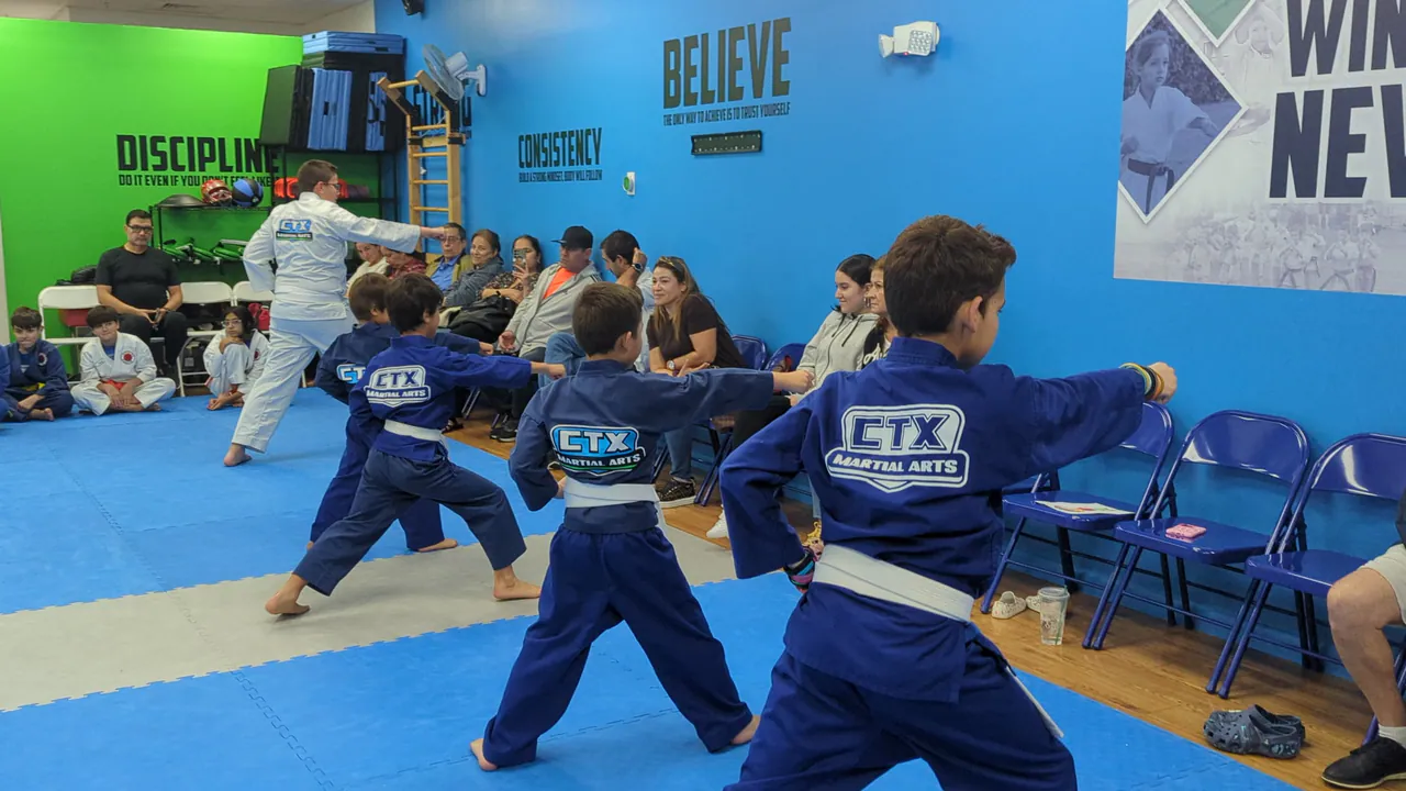 Kids in blue uniforms practicing karate punches in a low stance during class
