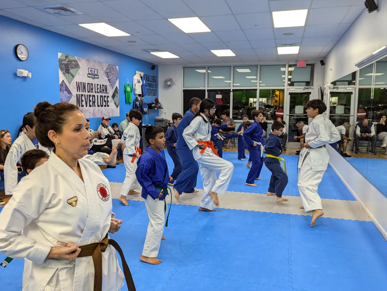 Students practicing karate techniques on blue mats while an instructor supervises