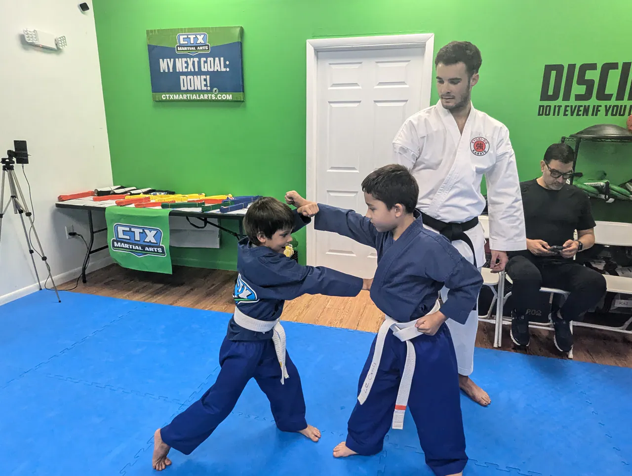 Two kids doing a supervised karate partner drill with an instructor beside them
