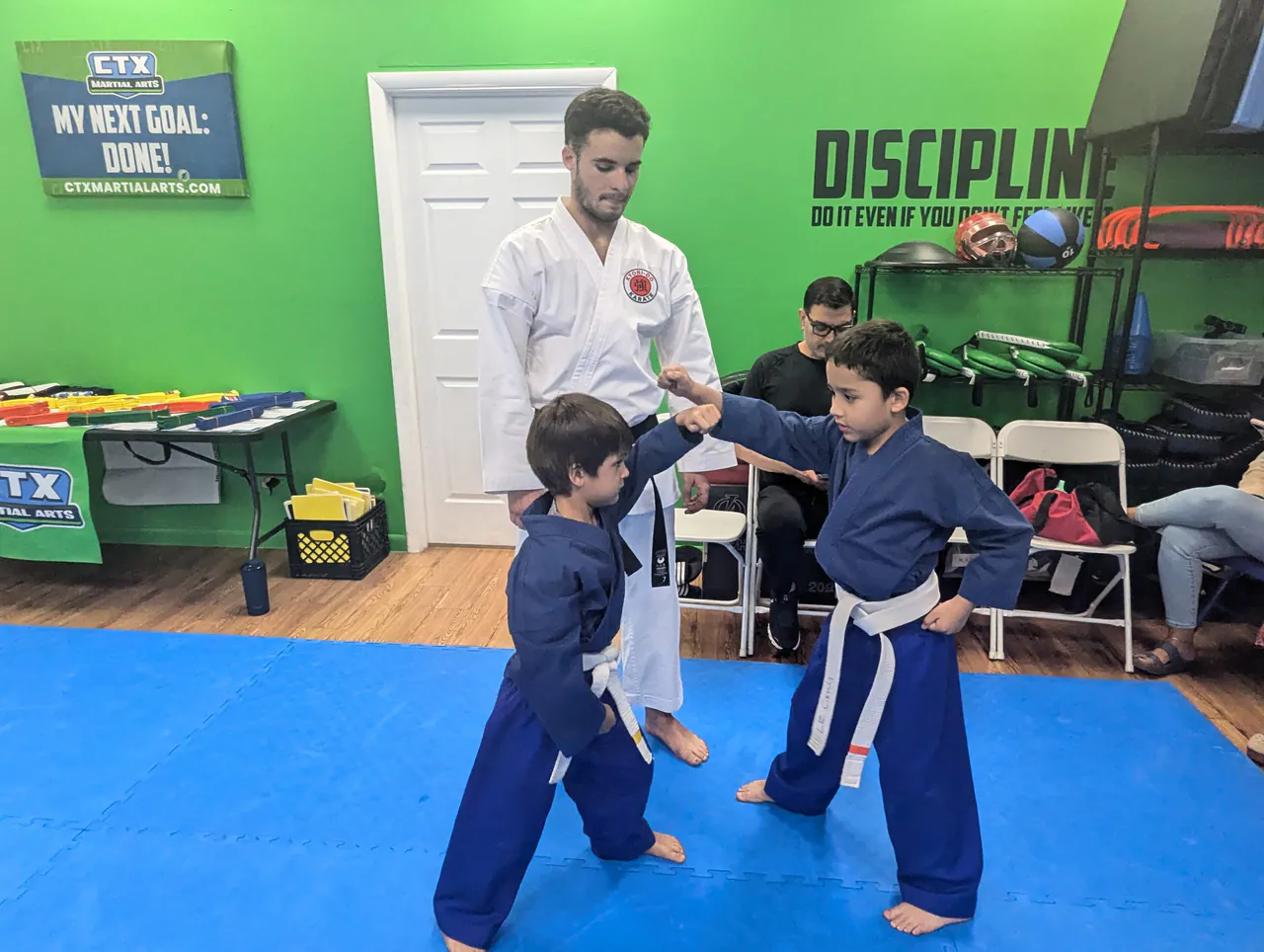 Young beginner practicing a karate drill with a partner while an instructor guides them